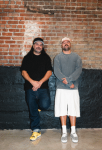 Laurent Dagenais et Phil Grisé posent devant le mur de brique dans la future boutique Empire Montréal, Quartier Latin.