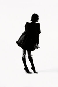 Silhouette of a person in a short dress with a cape and knee-high heeled boots, posing on a white background.