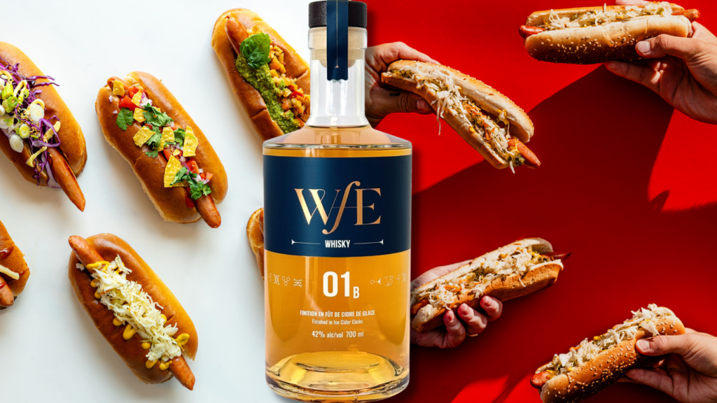 WE Whisky bottle centered among colorful loaded hot dogs on a white and red background, suggesting pairing or promotion.