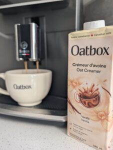 Emballages des nouveaux crémeurs à café d'avoine Oatbox saveurs vanille et chocolat noir entourés d'ingrédients naturels.