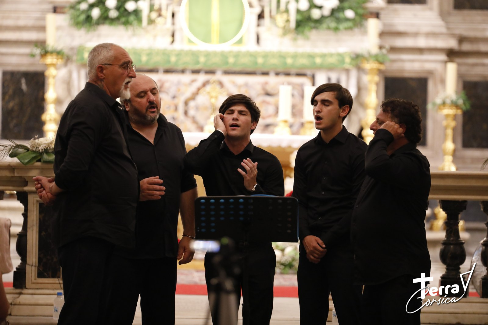 5 chanteurs en cercle autour d'un micro dans une église