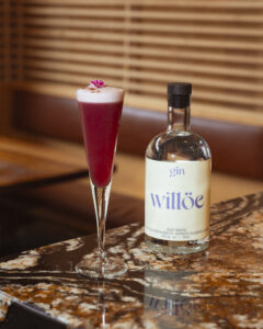 Cocktail festif coloré réalisé avec le gin montréalais willöe présenté à côté de sa bouteille référence au fichier Crédit Photo @Etienne Bay